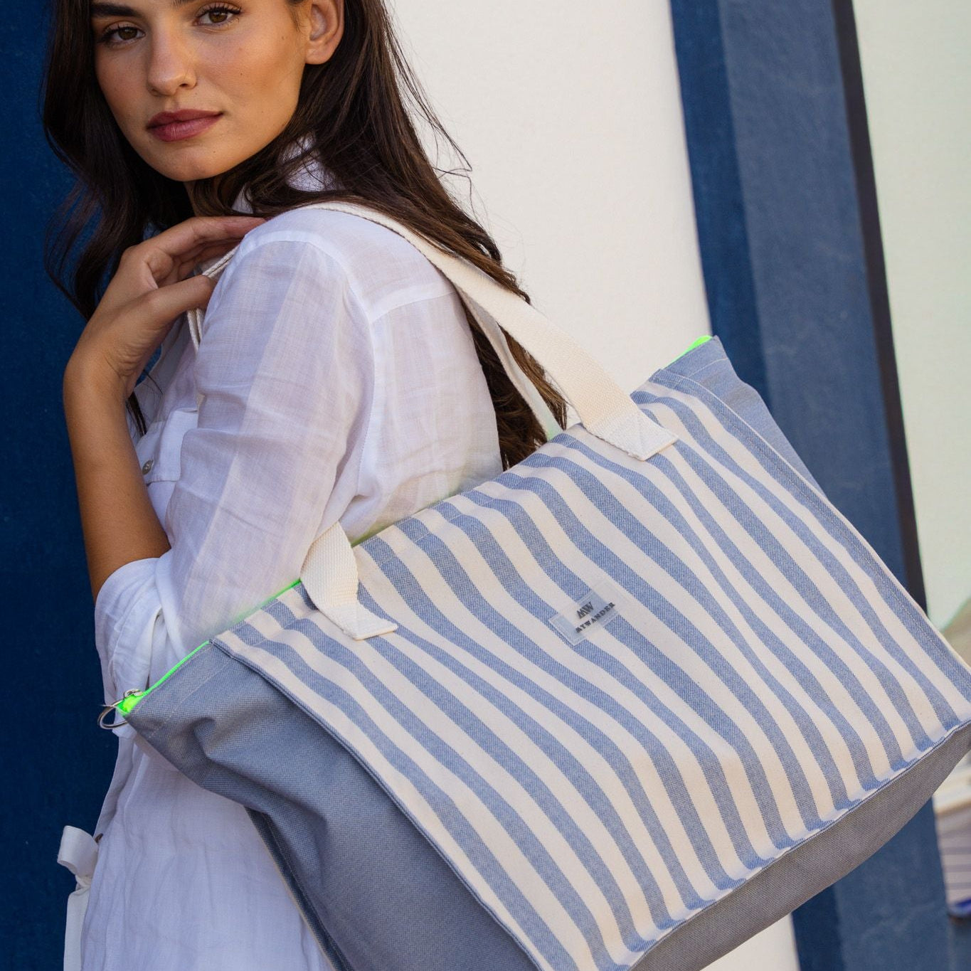Bolso de viaje mediano a rayas azul marino y blanco con cremallera en amarillo flúor, colgado al hombro.
